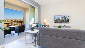 A modern living room with a grey sofa, a dining table with chairs, a TV mounted on the wall, and a balcony with a view. - Chic 2Bd Family Retreat With Free Waterpark (Davenport)