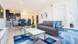 A modern living room with a grey sofa, a coffee table, and a dining area with chairs and a table. - Chic 2Bd Family Retreat With Free Waterpark (Davenport)