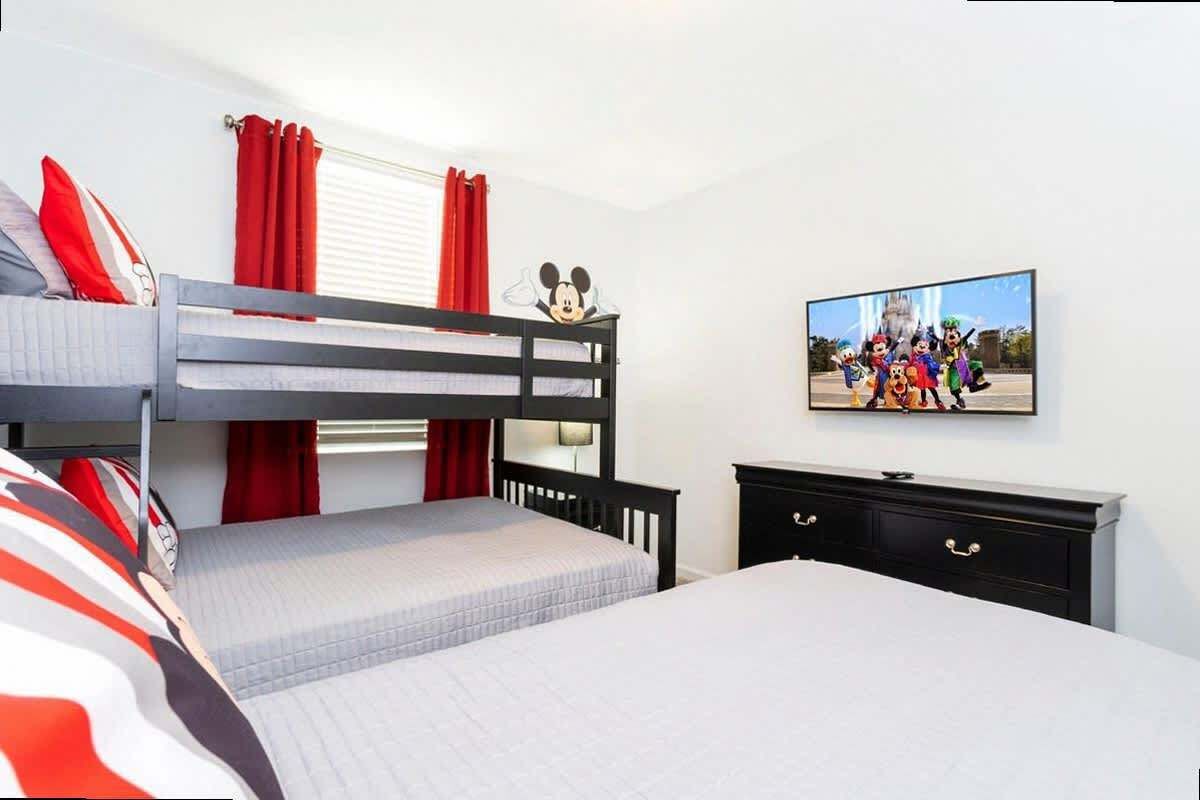 A bunk bed room with a television on the wall and a Disney-themed decoration.