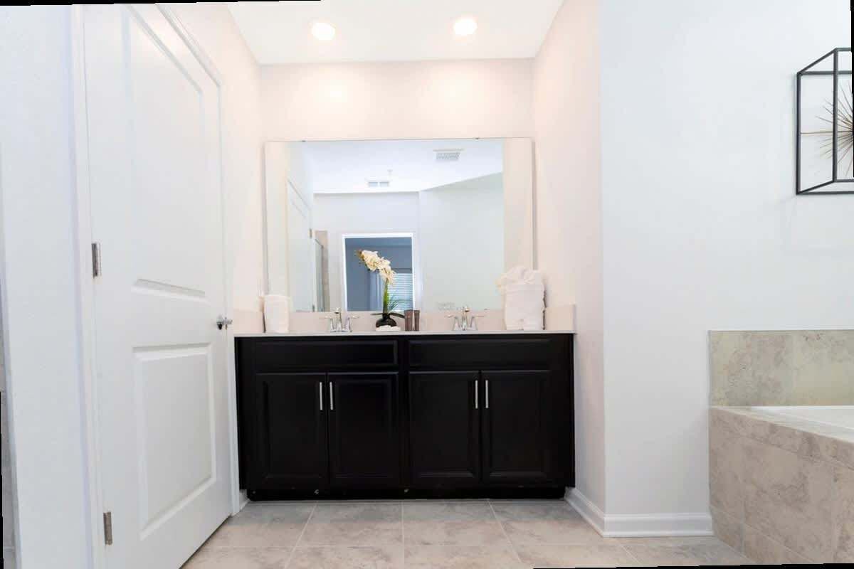 Un baño moderno con armarios oscuros, un espejo grande y un lavabo de mármol.