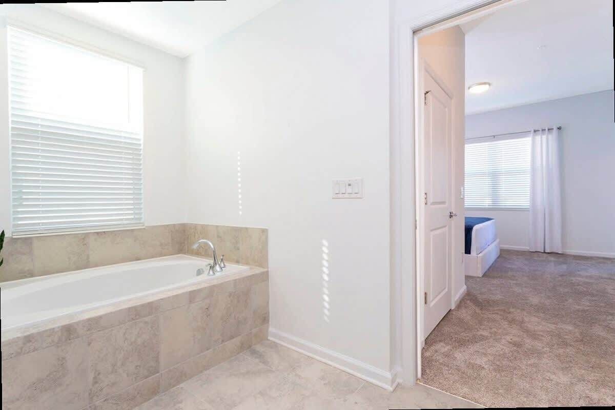 Casa de banho com banheira, janela com persianas e porta para outro quarto.