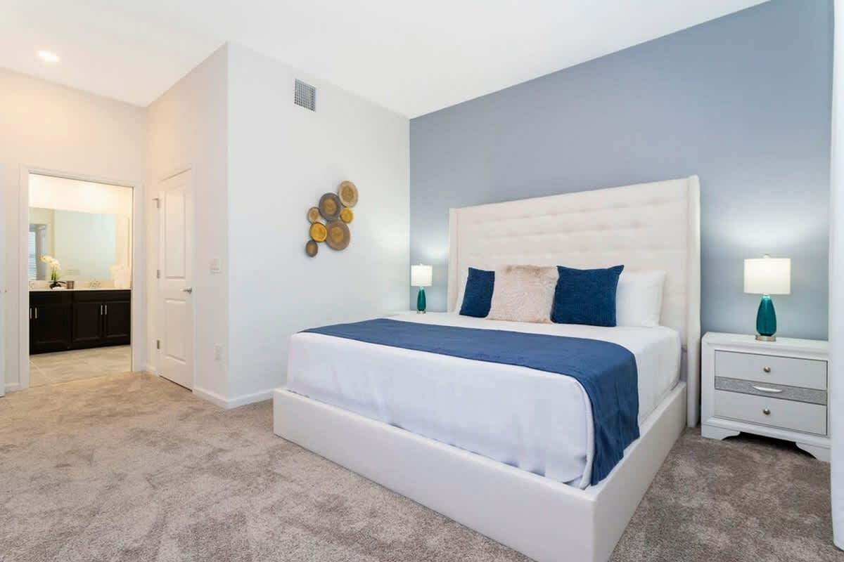 A bedroom with a large bed, a nightstand, a wall-mounted lamp, and a door leading to a bathroom.