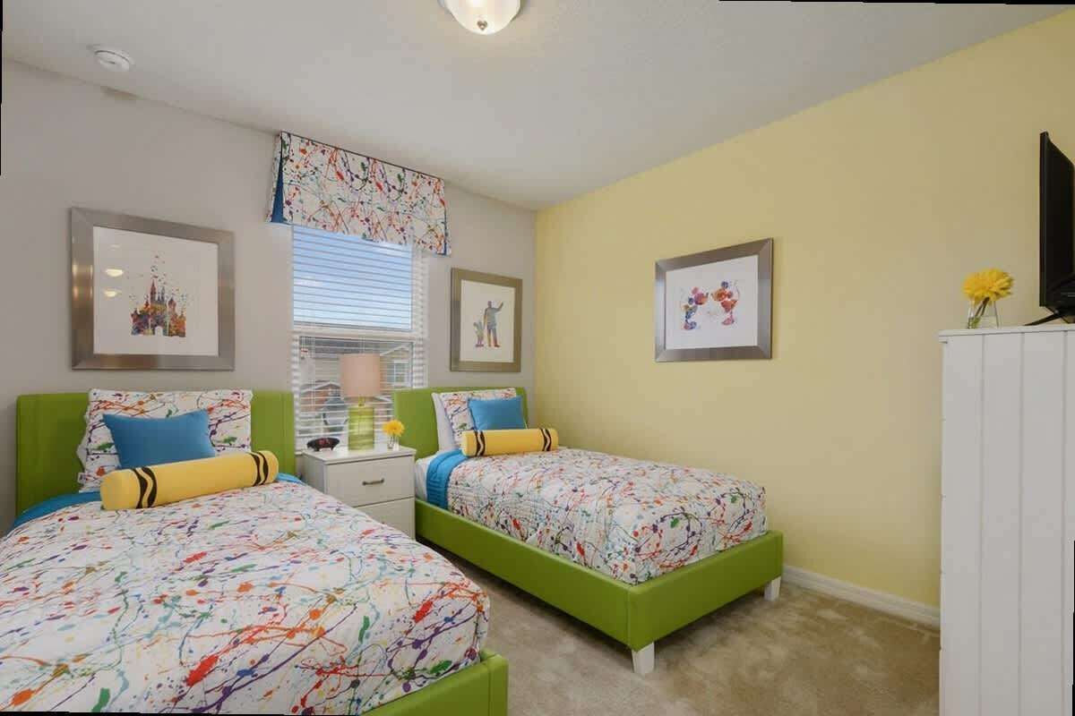 A bedroom with two green beds, a nightstand, a lamp, and framed pictures on the walls.