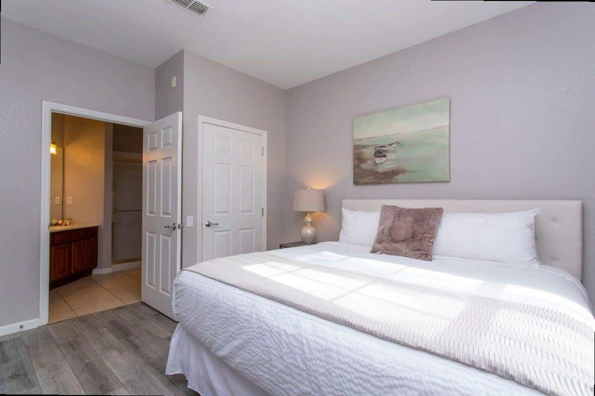 Een slaapkamer met een groot bed, nachtkastje, lamp, schilderij aan de muur en een kast.