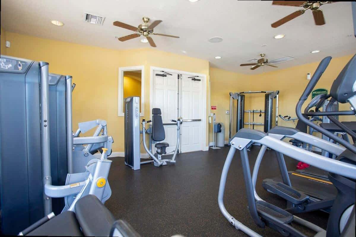 Un gimnasio con equipo de ejercicio, ventiladores de techo y una puerta que da a otra habitación.
