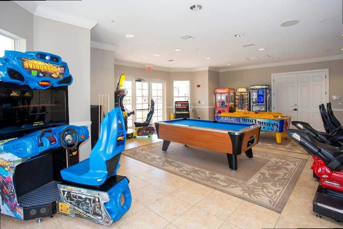 Una habitación con mesa de billar, juegos de arcade y equipo de ejercicio.