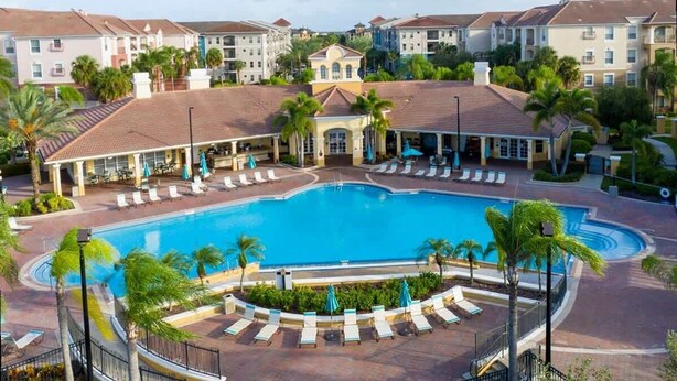 Ein Resort mit einem zentralen Schwimmbecken, Liegebereichen mit Sonnenliegen und einer Kulisse aus mehrstöckigen Gebäuden.