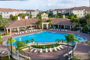 A resort with a central swimming pool, lounge areas with sun loungers, and a backdrop of multi-story buildings. - Spacious 2Bd Condo - Pool Hot Tub - Near I-drive (Orlando)
