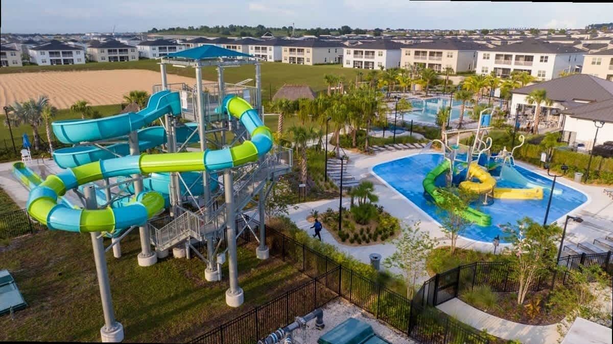 A water park with multiple slides and a swimming pool, surrounded by a landscaped area and residential buildings.