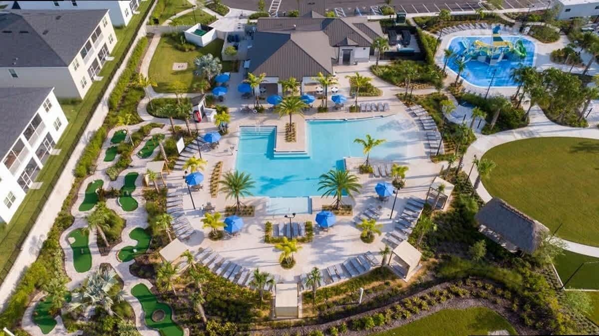 Vista aérea de un resort con una piscina central, tumbonas, palmeras y un parque acuático.