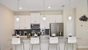 A modern kitchen with white cabinets, stainless steel appliances, and a central island with bar stools. - Bright 4Bd With Pool Resort Perks Near Disney (Kissimmee)