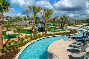 A swimming pool area with palm trees, lounge chairs, and a golf course.