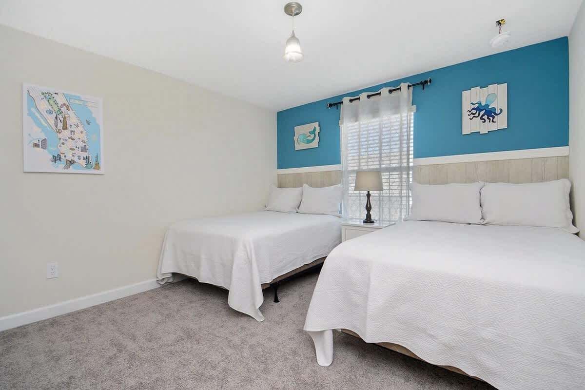 A bedroom with two beds, a nightstand, a lamp, and a window with curtains.