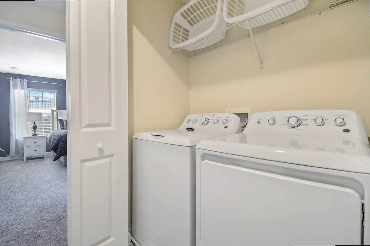 A laundry room with two front-loading washing machines and a drying rack above.
