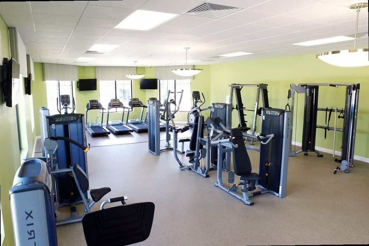 Ein Fitnessstudio mit verschiedenen Trainingsgeräten, Laufbändern und einer Spiegelwand.