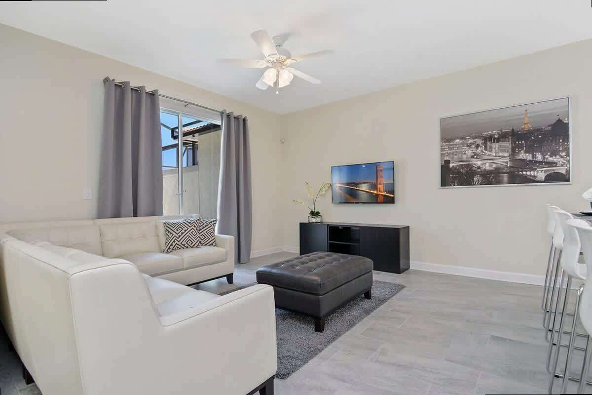 A modern living room with a sofa, ottoman, and a flat-screen TV mounted on the wall.