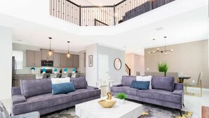 A modern living room with two grey sofas, a white coffee table, and a dining area with a table and chairs.