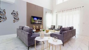 A modern living room with two grey sofas, a white coffee table, and a flat-screen TV mounted on a wooden panel.