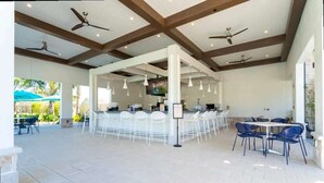 A spacious outdoor area with a bar, white chairs, and ceiling fans.