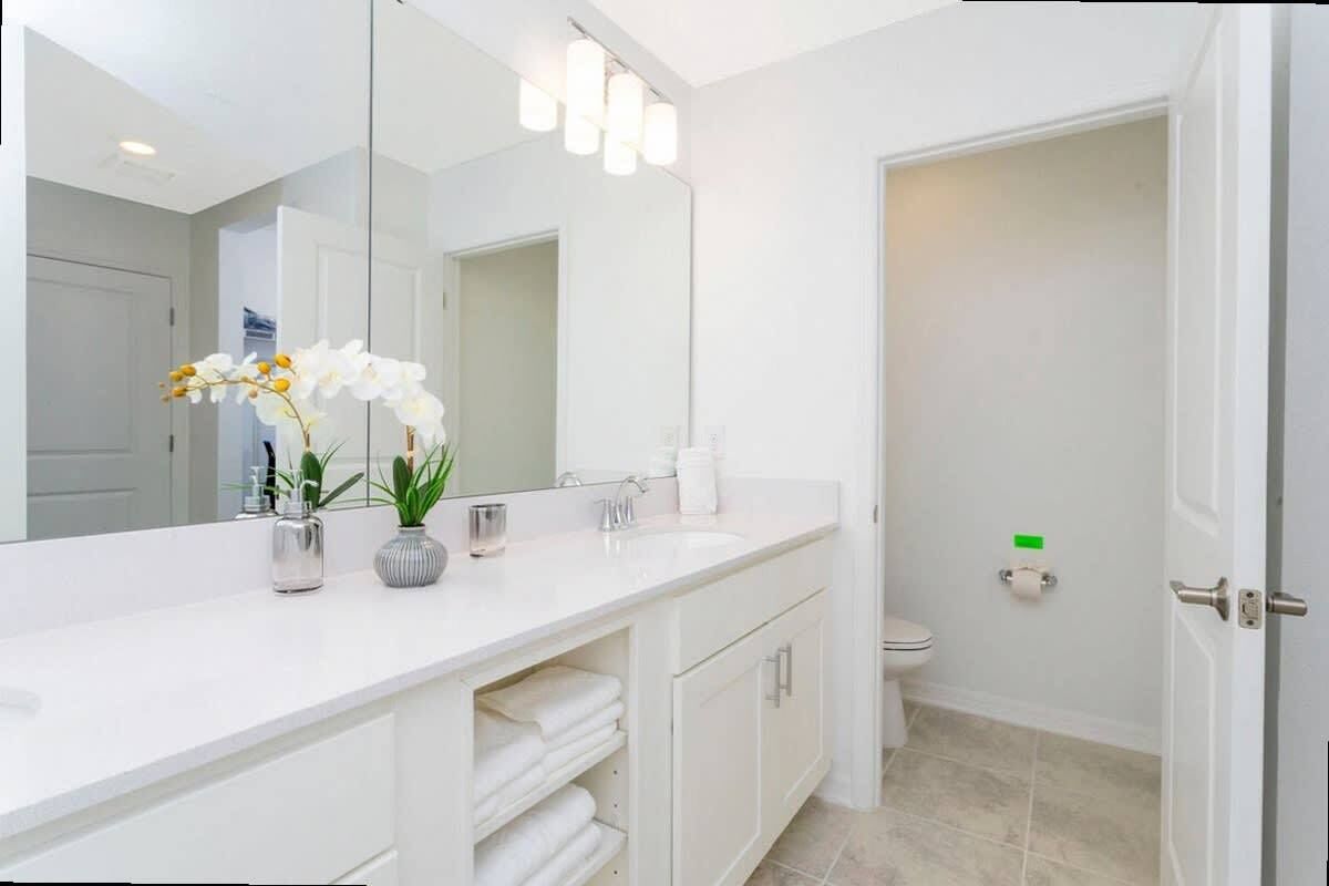 A modern bathroom with a white vanity, a large mirror, and a toilet.
