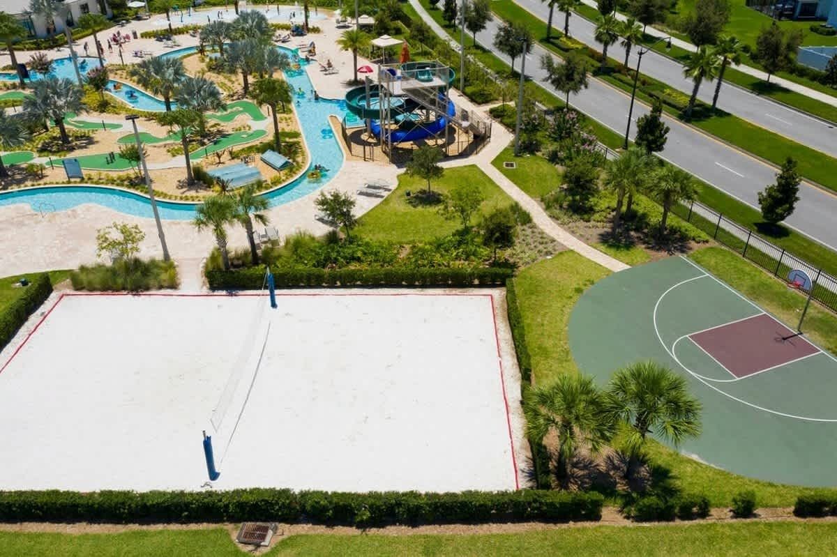 Una amplia piscina al aire libre con tobogán de agua, rodeada de palmeras y una cancha de baloncesto.