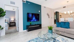 Een moderne woonkamer met een turquoise accentmuur, een flatscreen televisie, een glazen salontafel en een beige bank.