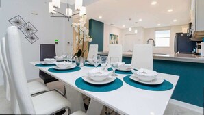 Een eetruimte met een witte tafel gedekt voor zes personen, teal placemats en witte borden.