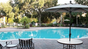 A swimming pool with lounge chairs and an umbrella, surrounded by trees and a brick patio. - Resort 4Bd Townhome w Gameroom Patio Near Disney (Kissimmee)