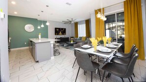 Eine moderne Küche mit einer zentralen Kochinsel, einem Essbereich mit Tisch für vier Personen und einem Wohnbereich mit Sofa und Fernseher.