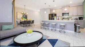 Eine moderne Küche mit Edelstahlgeräten, ein Essbereich mit Tisch und Stühlen sowie ein Wohnzimmer mit Sofa und Couchtisch.