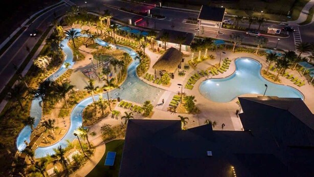 Vue aérienne d’un complexe hôtelier avec des piscines sinueuses, des palmiers et une structure surmontée d’un toit de chaume.