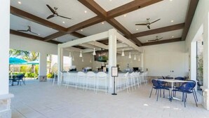 Un vaste espace extérieur doté d’un bar, de chaises blanches et de ventilateurs de plafond.