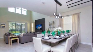 A modern living room with a dining area, a sofa, a TV, and a view of the outdoors. - Family 5BD Spa Pool Game Loft Near Disney (Kissimmee)