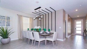 A dining area with a rectangular table, six chairs, a potted plant, and a modern chandelier. - Family 5BD Spa Pool Game Loft Near Disney (Kissimmee)