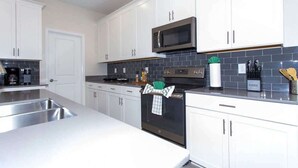 A modern kitchen with white cabinets, a stainless steel sink, a microwave, and a stove. - Family 5BD Spa Pool Game Loft Near Disney (Kissimmee)