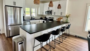 Een moderne keuken met witte kasten, roestvrijstalen apparatuur, een centraal eiland met barstoelen en hangende吊り下げ照明.