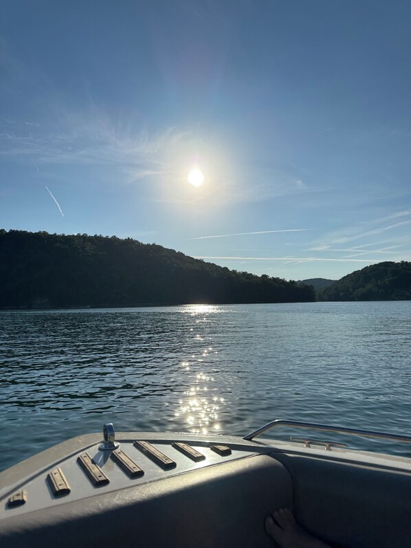 Un bote sobre aguas tranquilas, cielo despejado y sol reflejado en la superficie.