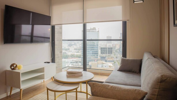 Ein modernes Wohnzimmer mit einer Couch, einem runden Tisch und einem an der Wand befestigten Fernseher.