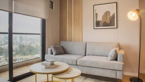 Ein modernes Wohnzimmer mit einem grauen Sofa, einem runden Couchtisch und einer Stehlampe. Ein gerahmtes Stadtbild hängt an der Wand.