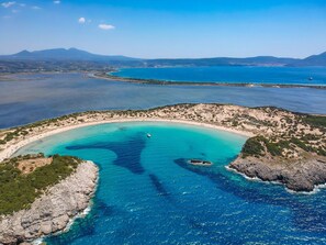 An aerial view of a coastal area with clear turquoise waters, rocky terrain, and distant mountains.