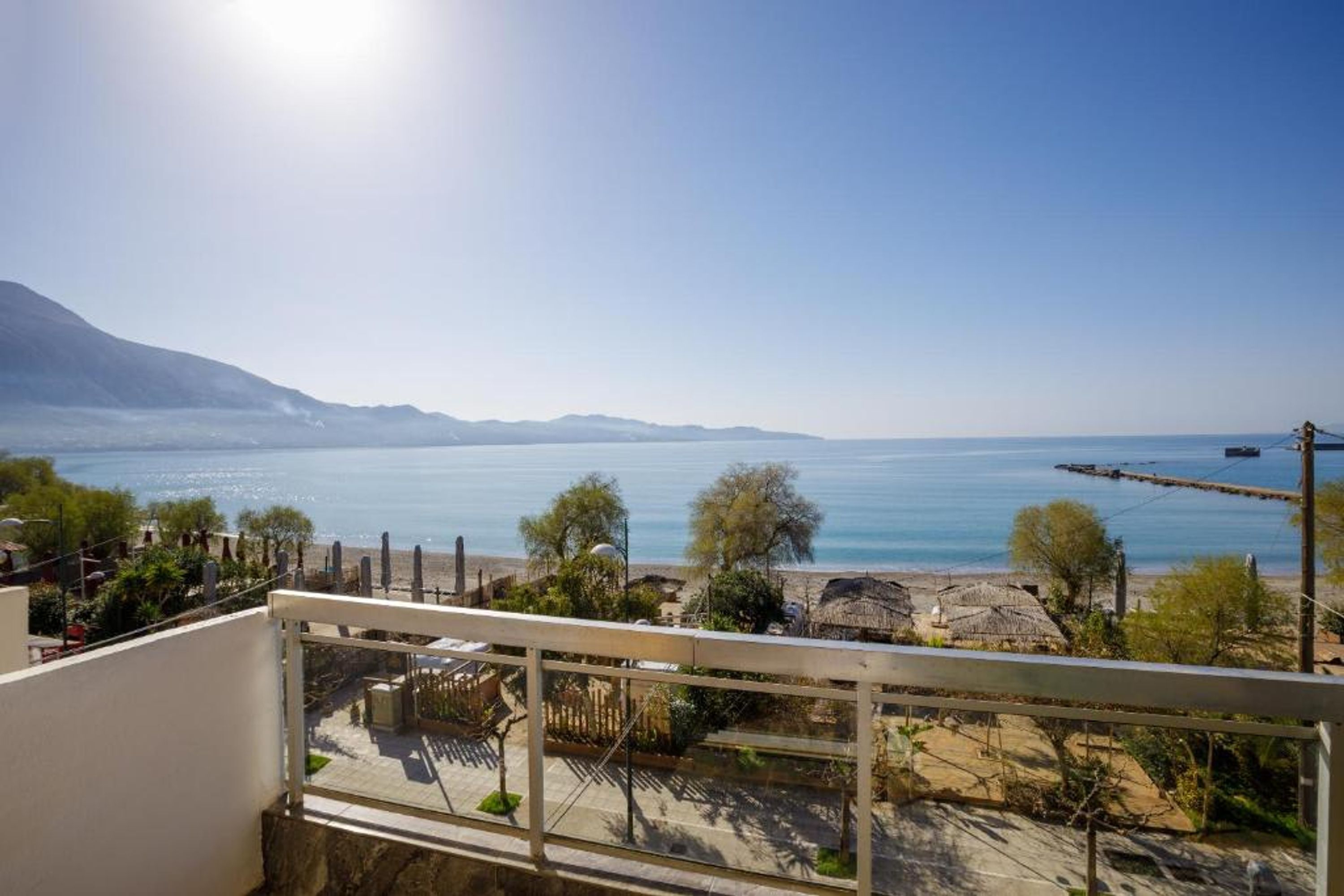 A balcony overlooking a beach with a clear view of the sea and distant mountains.
