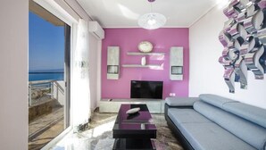 A modern living room with a large window, a flat-screen TV, a sofa, and decorative wall art. - Kalamata Coastal Charm Modern Seaside Escape (Kalamata)