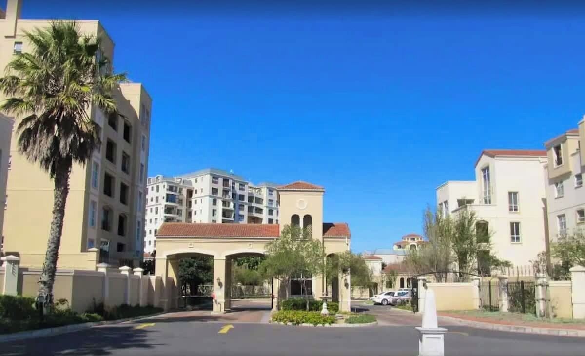 A multi-story residential building with a central archway entrance, palm trees, and a clear blue sky.