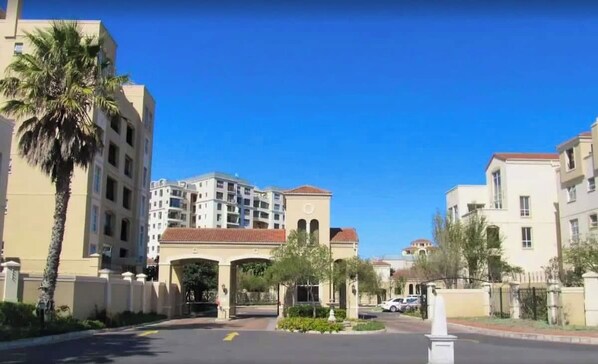 A multi-story residential building with a central archway entrance, palm trees, and a clear blue sky. - 2 Bedroom Mountain View Penthouse Century City (Cape Town)