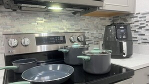Une cuisine avec un poêle noir, deux casseroles, une poêle et une machine à café.