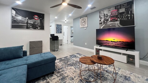 Un salon moderne doté d’un grand téléviseur à écran plat, d’un ventilateur de plafond et d’un canapé bleu.