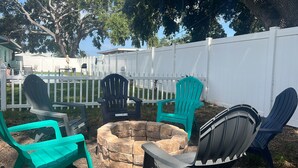 Un jardin avec un foyer en pierre, plusieurs fauteuils Adirondack et une clôture blanche.