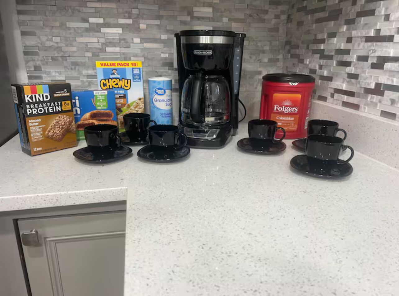 Una encimera de cocina con alimentos para el desayuno, cafetera y café Folgers.