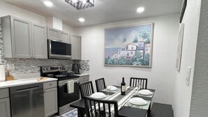 Une cuisine moderne avec des meubles gris, un four à micro-ondes, une cuisinière et un coin repas aménagé pour quatre personnes, avec une table, des chaises et un tableau accroché au mur.