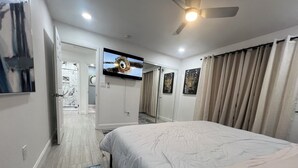 Une chambre d’hôtel dotée d’un grand lit, d’un ventilateur de plafond, d’un téléviseur à écran plat fixé au mur et d’une porte donnant accès à une salle de bain.